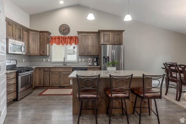 kitchen with appliances with stainless steel finishes, a sink, a kitchen island, dark wood finished floors, and high vaulted ceiling