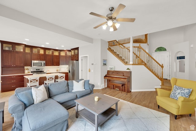 living room featuring stairway, light wood-type flooring, ceiling fan, baseboards, and recessed lighting