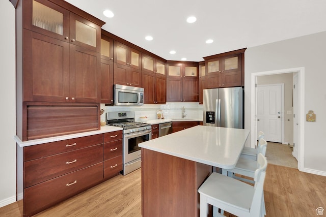 kitchen with stainless steel appliances, a sink, decorative backsplash, light countertops, and a kitchen bar