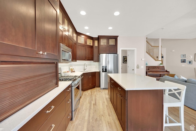 kitchen with appliances with stainless steel finishes, a sink, light wood-type flooring, a kitchen breakfast bar, and recessed lighting