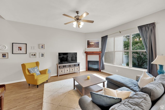 living area with wood finished floors, a ceiling fan, baseboards, and a glass covered fireplace