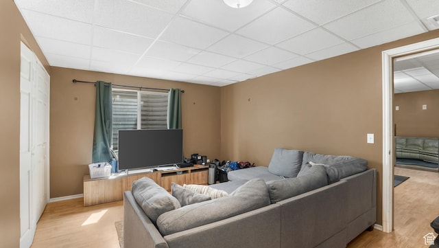 living area featuring a paneled ceiling, light wood-style flooring, and baseboards
