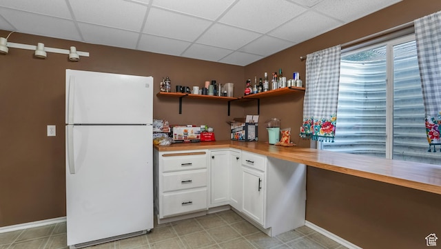 kitchen with freestanding refrigerator, a drop ceiling, open shelves, white cabinets, and baseboards