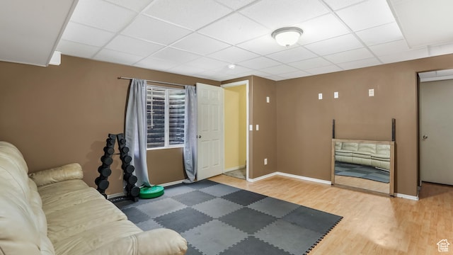 living area featuring a drop ceiling, wood finished floors, and baseboards