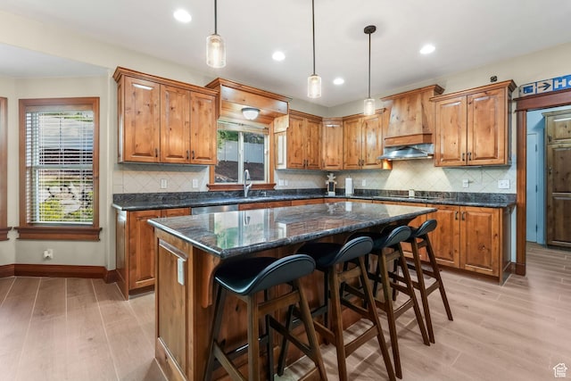 kitchen featuring brown cabinets, light wood-style floors, a center island, a sink, and recessed lighting
