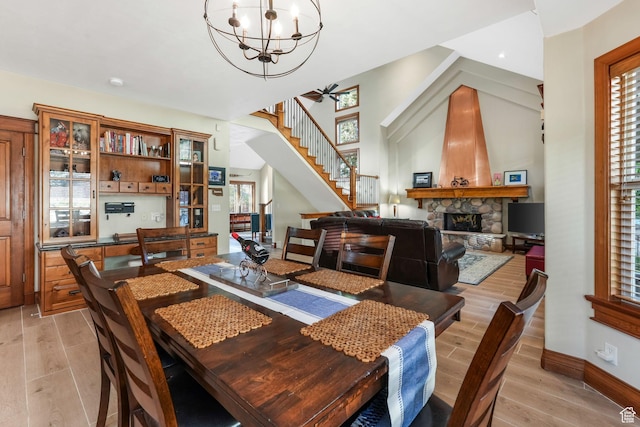 dining room with stairs, a fireplace, light wood-style flooring, a chandelier, and plenty of natural light
