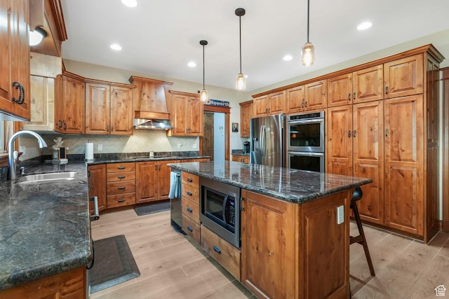 kitchen featuring stainless steel appliances, a sink, a center island, light wood-style floors, and recessed lighting