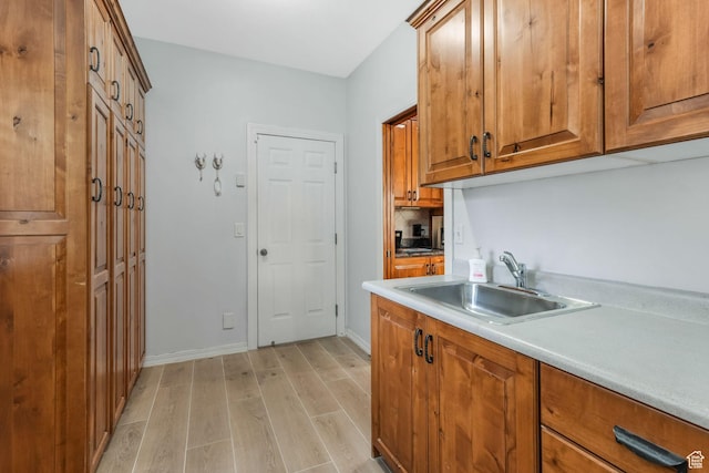 kitchen with a sink, brown cabinetry, light wood-style floors, baseboards, and light countertops