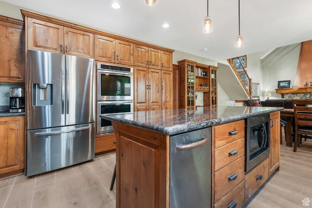kitchen featuring stainless steel appliances, dark stone counters, light wood-type flooring, brown cabinets, and recessed lighting
