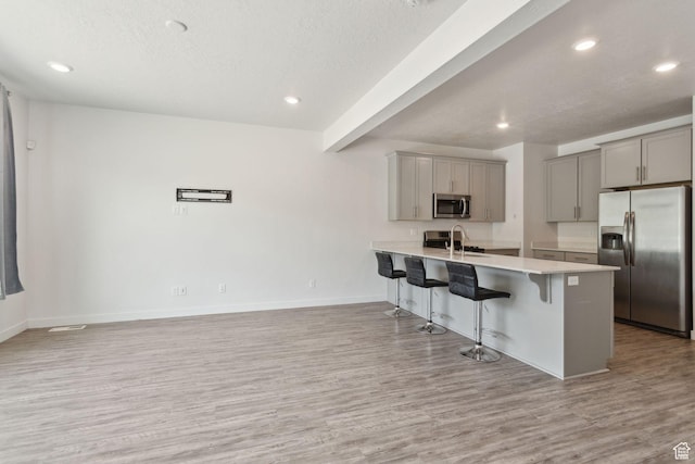 3714 W Soft Whisper Way, Herriman, UT 84096 - kitchen featuring stainless steel appliances, gray cabinetry, a breakfast bar, light wood-type flooring, and a peninsula