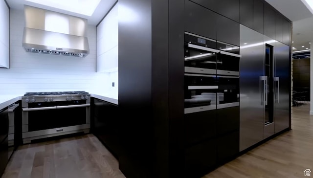 422 N Castor Ln, Salt Lake City, UT 84103 - kitchen with appliances with stainless steel finishes, modern cabinets, light wood finished floors, wall chimney range hood, and dark cabinets
