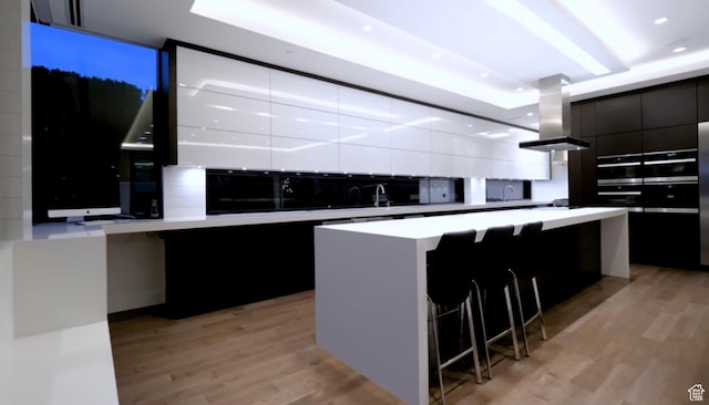 422 N Castor Ln, Salt Lake City, UT 84103 - kitchen featuring modern cabinets, island range hood, light wood-style floors, a center island, and dark cabinets