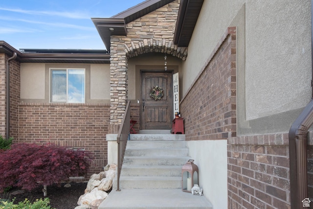 view of exterior entry with stucco siding and brick siding