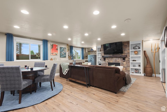 living area featuring recessed lighting, light wood-type flooring, a stone fireplace, and baseboards