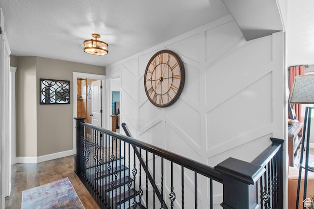 hallway featuring an upstairs landing, wood finished floors, baseboards, and a textured ceiling