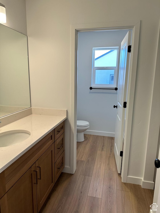 bathroom with wood finished floors, toilet, vanity, and baseboards