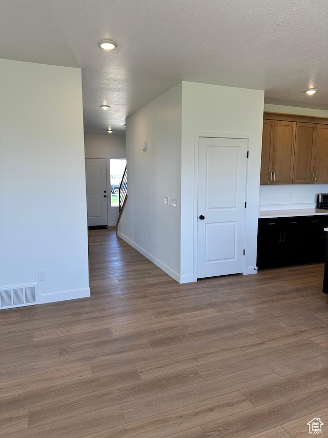 unfurnished room with baseboards, light wood-style flooring, a textured ceiling, stairs, and recessed lighting