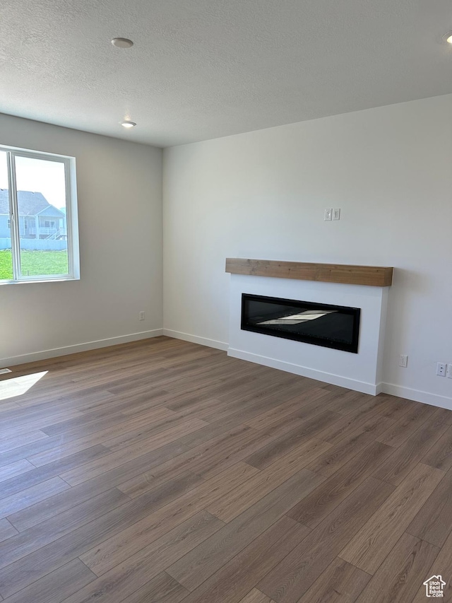 unfurnished living room with a glass covered fireplace, wood finished floors, baseboards, a textured ceiling, and recessed lighting
