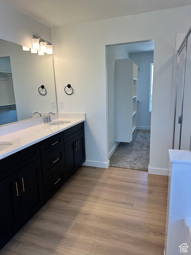 full bath featuring wood finished floors, double vanity, and baseboards