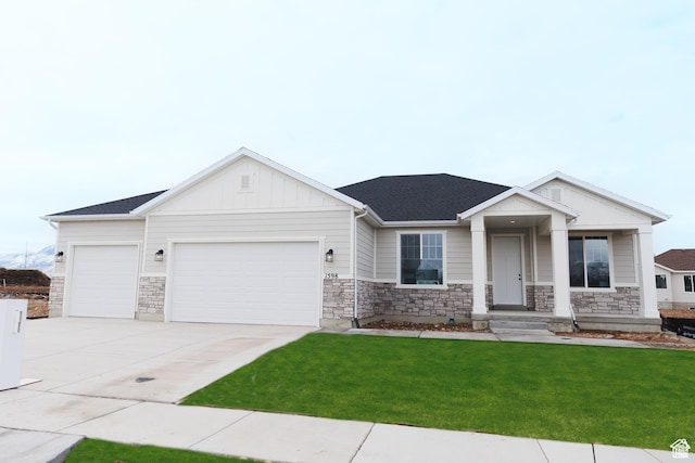 view of front of house featuring an attached garage, a front yard, driveway, stone siding, and board and batten siding