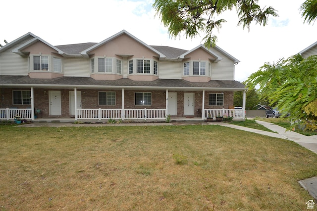 view of property with a porch, brick siding, a front lawn, and roof with shingles