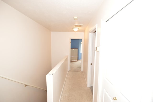 hallway with an upstairs landing, light colored carpet, and baseboards