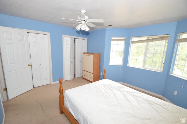 carpeted bedroom with baseboards, multiple closets, and a ceiling fan