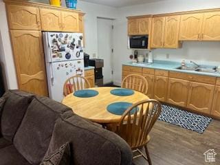 kitchen with freestanding refrigerator, built in microwave, wood finished floors, a sink, and light countertops