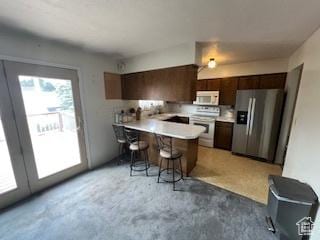kitchen featuring appliances with stainless steel finishes, a peninsula, a breakfast bar, light countertops, and concrete floors