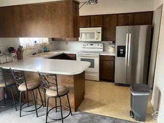 kitchen with white appliances, a peninsula, light countertops, and a breakfast bar area