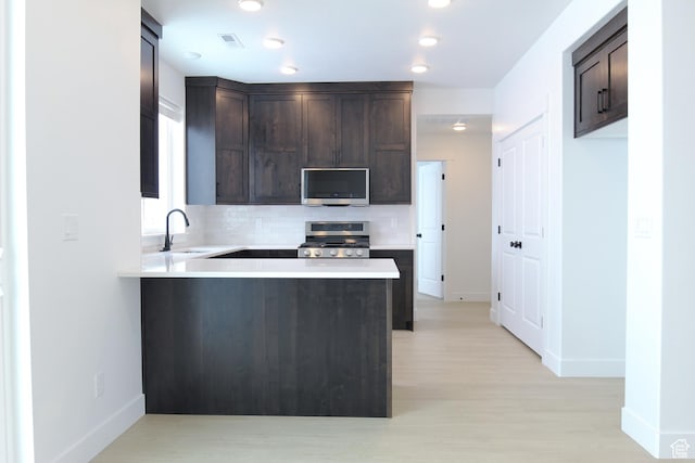 kitchen with gas stove, stainless steel microwave, dark brown cabinets, baseboards, and backsplash