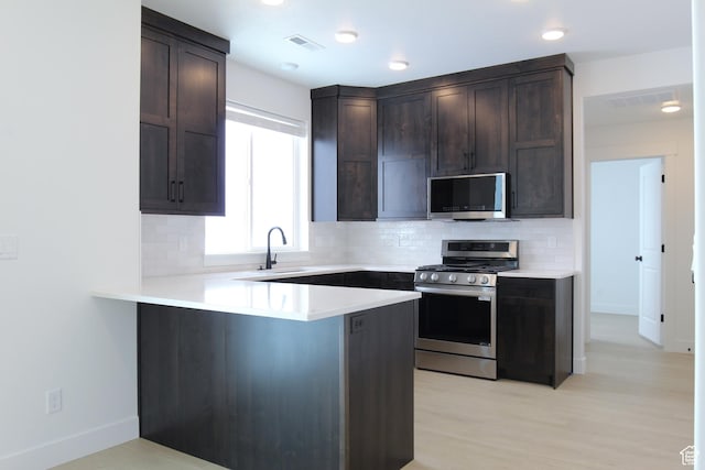 kitchen with stainless steel appliances, a sink, dark brown cabinets, tasteful backsplash, and a peninsula