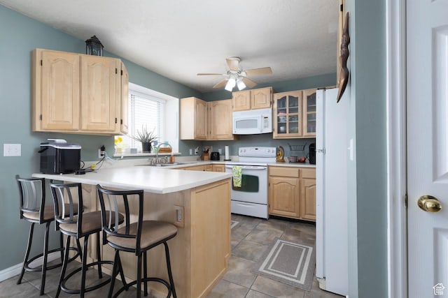 kitchen featuring white appliances, light brown cabinets, a sink, and a peninsula