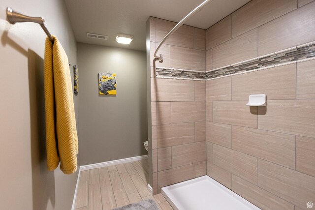 full bathroom with tiled shower, toilet, wood tiled floors, and baseboards