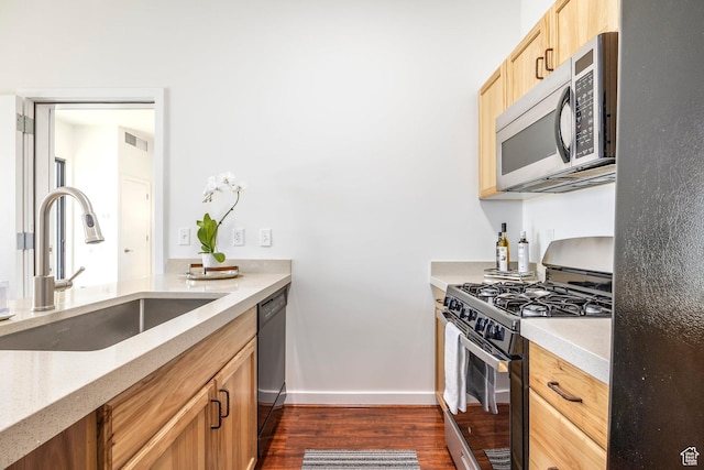 kitchen featuring stainless steel appliances, a sink, dark wood-type flooring, baseboards, and light stone countertops