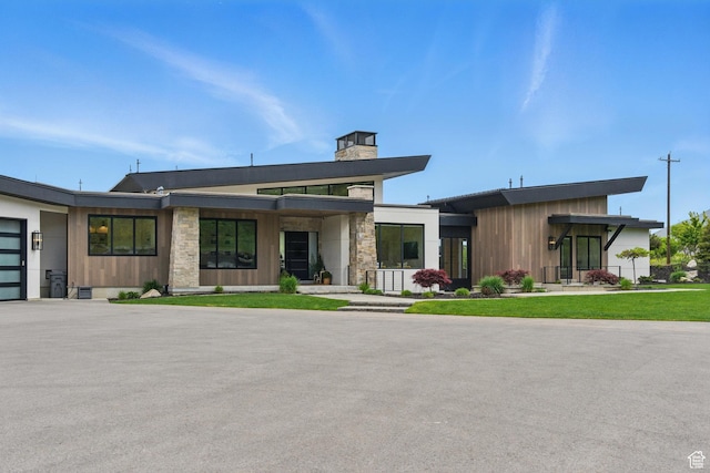 contemporary house with a chimney, stone siding, a garage, and asphalt driveway