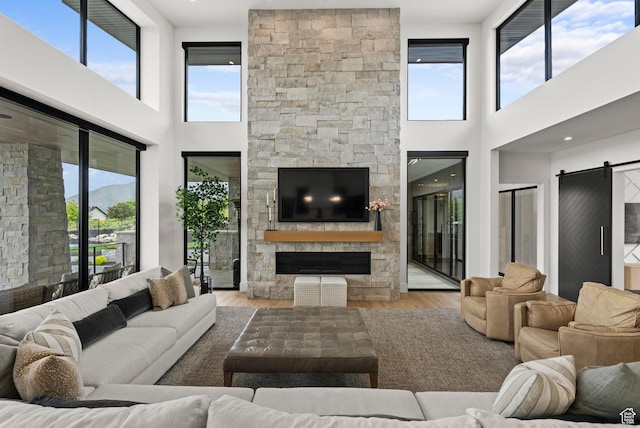 living area with a fireplace, a towering ceiling, a barn door, and wood finished floors