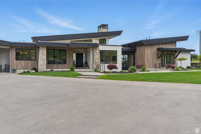 modern home with a chimney, stone siding, and a front lawn