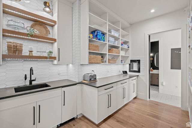 kitchen with open shelves, a sink, dark countertops, light wood-style flooring, and recessed lighting