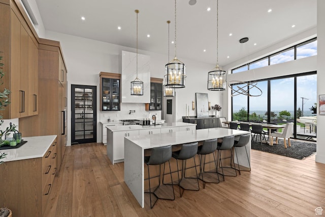 kitchen with a large island with sink, light wood finished floors, a chandelier, glass insert cabinets, and a kitchen breakfast bar