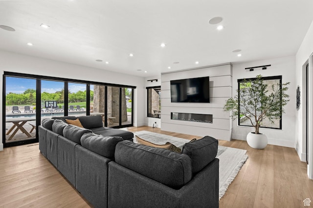 living area with recessed lighting, a glass covered fireplace, light wood-style flooring, and baseboards