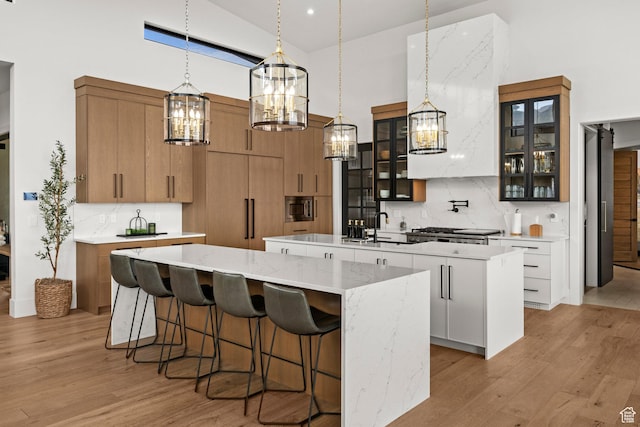 kitchen with a large island with sink, high vaulted ceiling, a chandelier, light wood finished floors, and stainless steel microwave