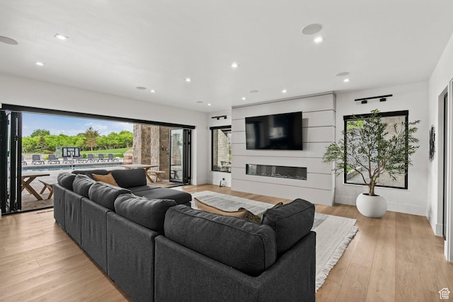 living area featuring a glass covered fireplace, light wood-type flooring, recessed lighting, and baseboards