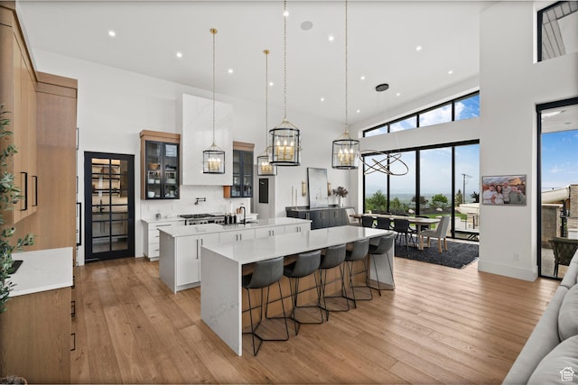 kitchen featuring a spacious island, a high ceiling, light wood-style flooring, light countertops, and glass insert cabinets