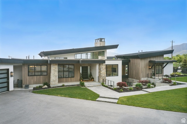 view of front of home featuring a chimney, a front yard, a porch, stone siding, and driveway
