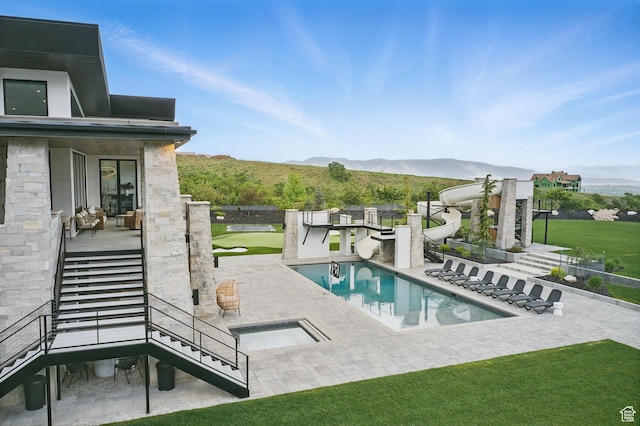 view of swimming pool featuring stairway, a patio, a mountain view, a water slide, and a lawn