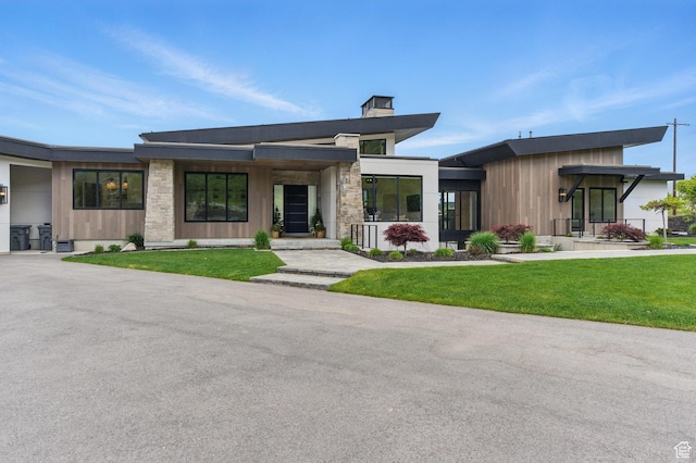 contemporary house featuring a front yard, a chimney, a porch, and stone siding