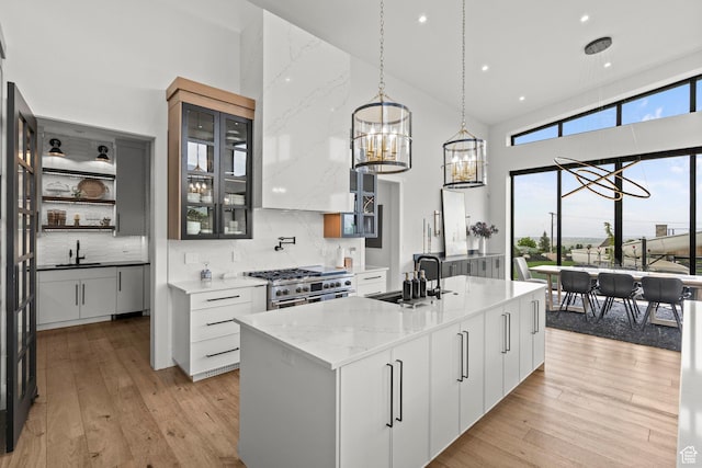 kitchen with a sink, a towering ceiling, a chandelier, high end stove, and light wood-type flooring