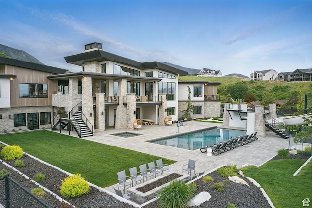 rear view of property featuring a balcony, a yard, stone siding, and an in-ground hot tub