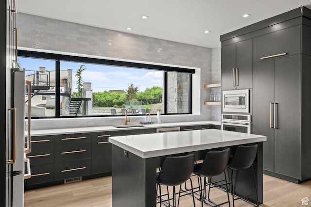 kitchen featuring stainless steel appliances, light countertops, a kitchen bar, light wood-style flooring, and recessed lighting